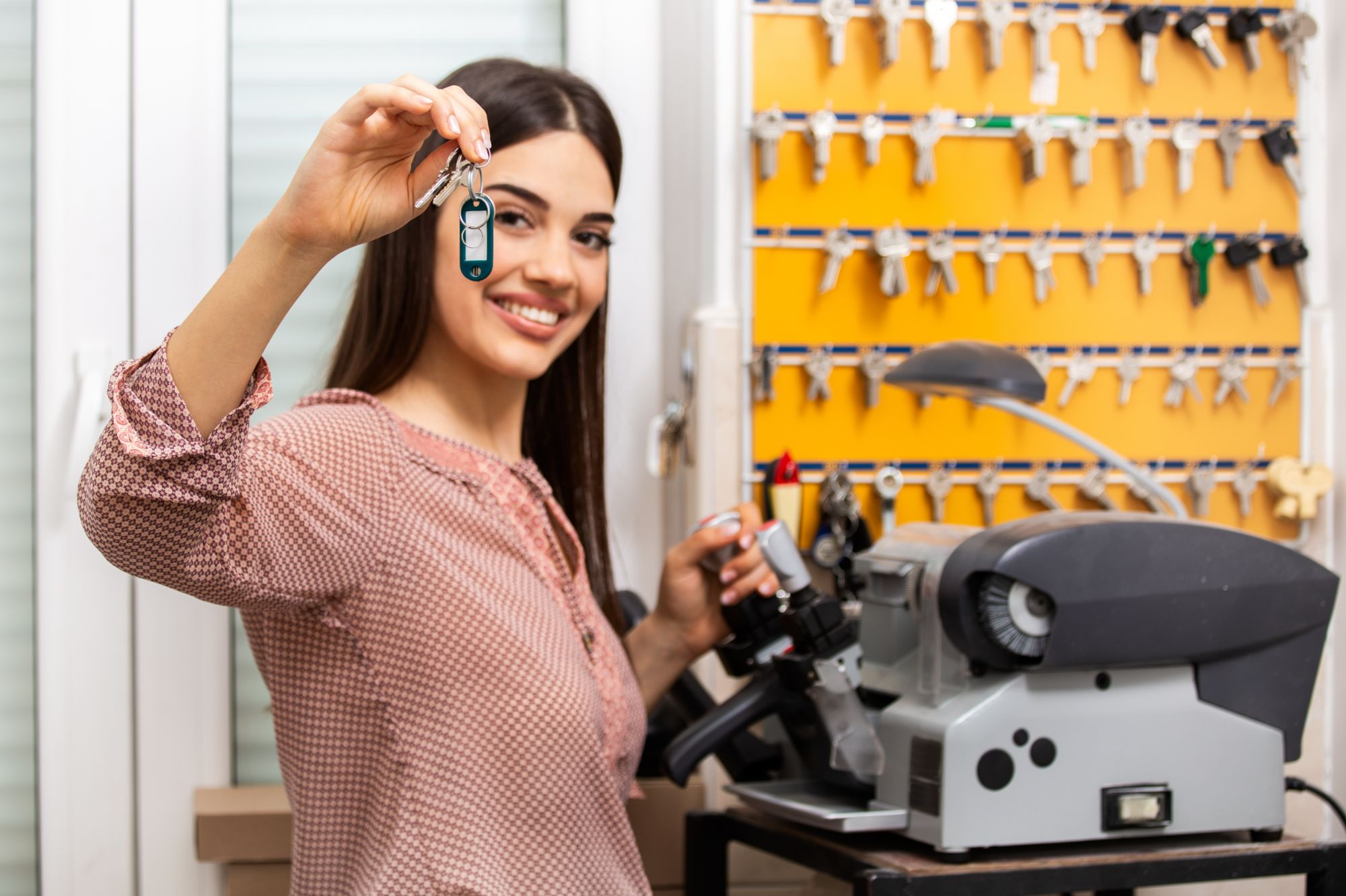 woman holding keys next to a key cutting machine